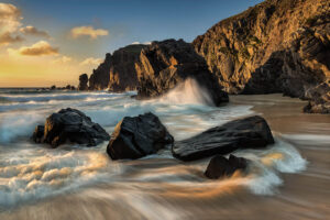 Streaked, bubbling and crashing waves flowing onto the Dalmore Beach at sunset, water moving around rocks in the foreground