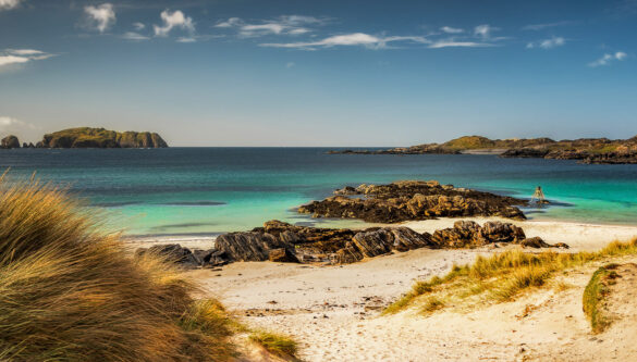 "Time and Tide Bell" at Bosta Beach on the rocks with aquamarine sea, blue clouds and wispy clouds.