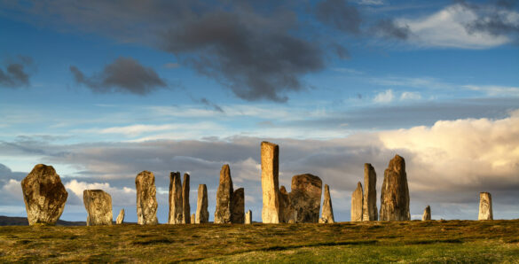 Ancient Callanish Standing Stones in a circle in sunlight against a sky of clouds.