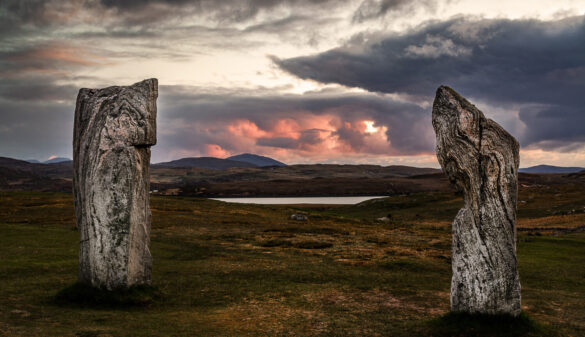 Two rocks of the Callanish Standing Stones facing each other as if in conversation, sunset with red and dark clouds.