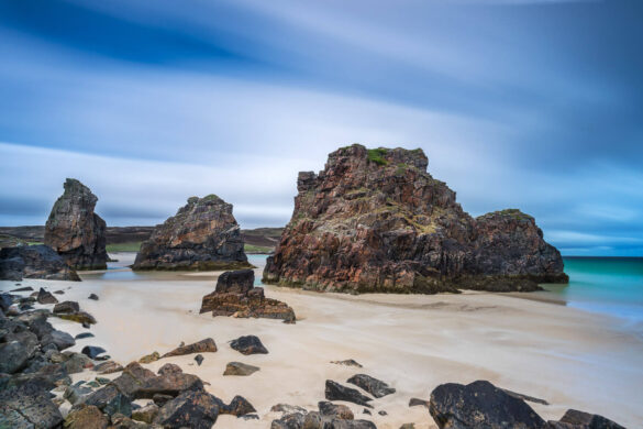 Garry Beach with red rocks, aquamarine sea, and blue sky with moody white and grey clouds.