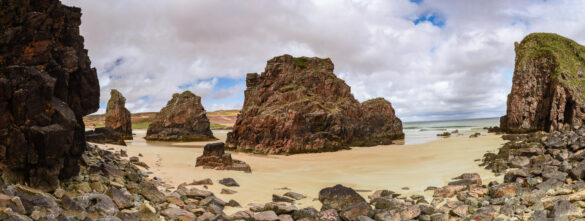 Panoramic view of Garry Beach with red and brown rocks and white cloudy sky.