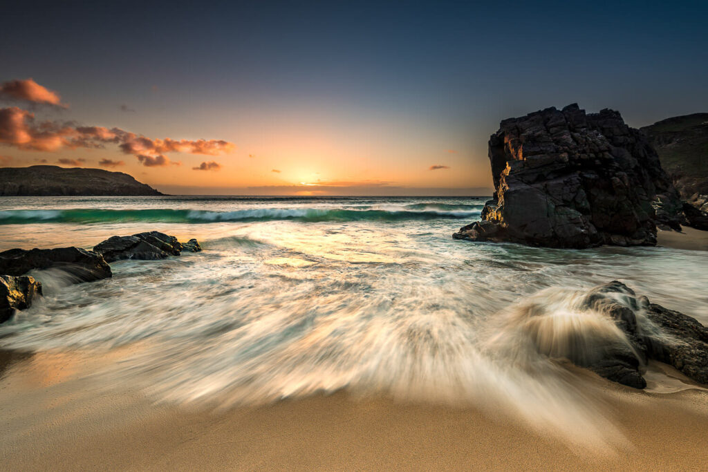 Sunset on Dalmore Beach, streaked waves, aquamarine sea, and the sun kissing the horizon with an inky blue sky.