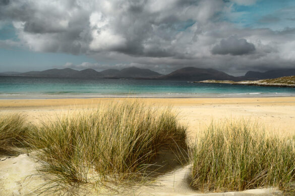 Luskentyre dunes with sandy dunes, yellow beach, aquamarine sea, and blue sky with moody white and grey clouds.