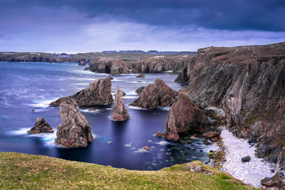 Mangersta sea stacks from above, monolith stacks, glassy water, and inky blue and white sky.