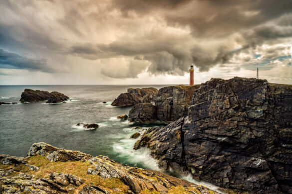 The Butt of Lewis with lighthouse on cliffs, sea crashing, and blue and tobacco sky with white clouds.