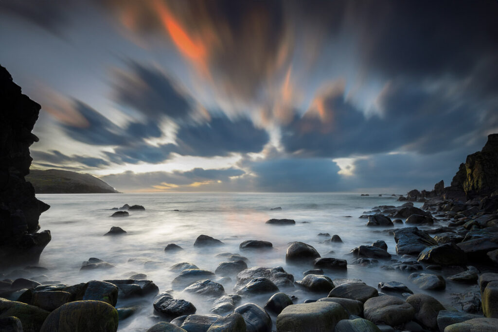 Dusk on Dalmore Beach, the misty sea swirling around rocks in the foreground.