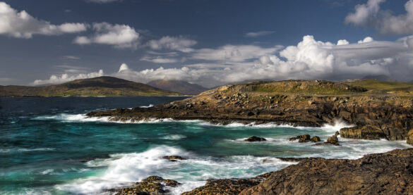 A view looking towards the Harris hills, rocky bay, and sky with aquamarine and inky blue tones.