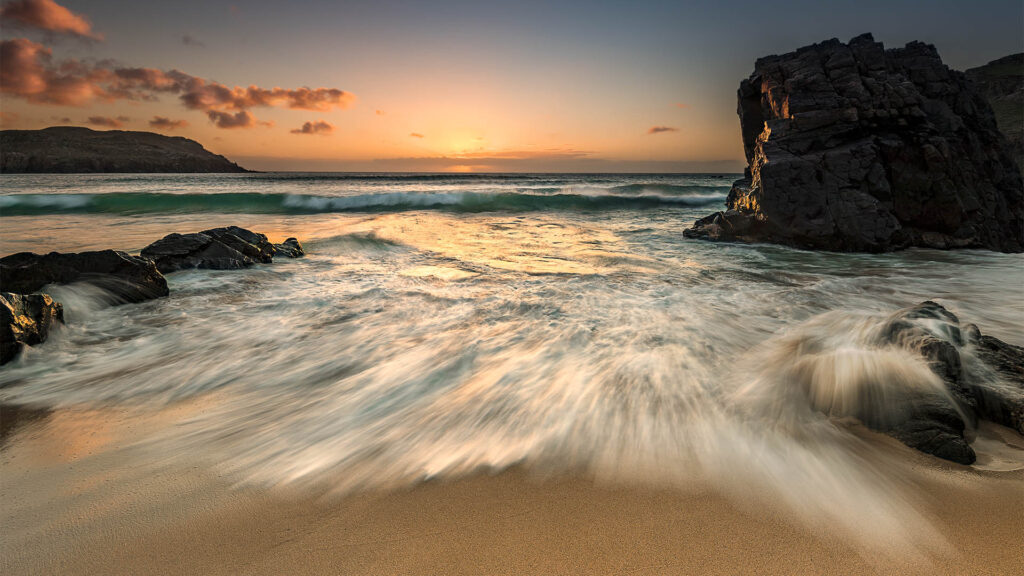 Sunset on Dalmore Beach, streaked waves, aquamarine sea, and the sun kissing the horizon with an inky blue sky.