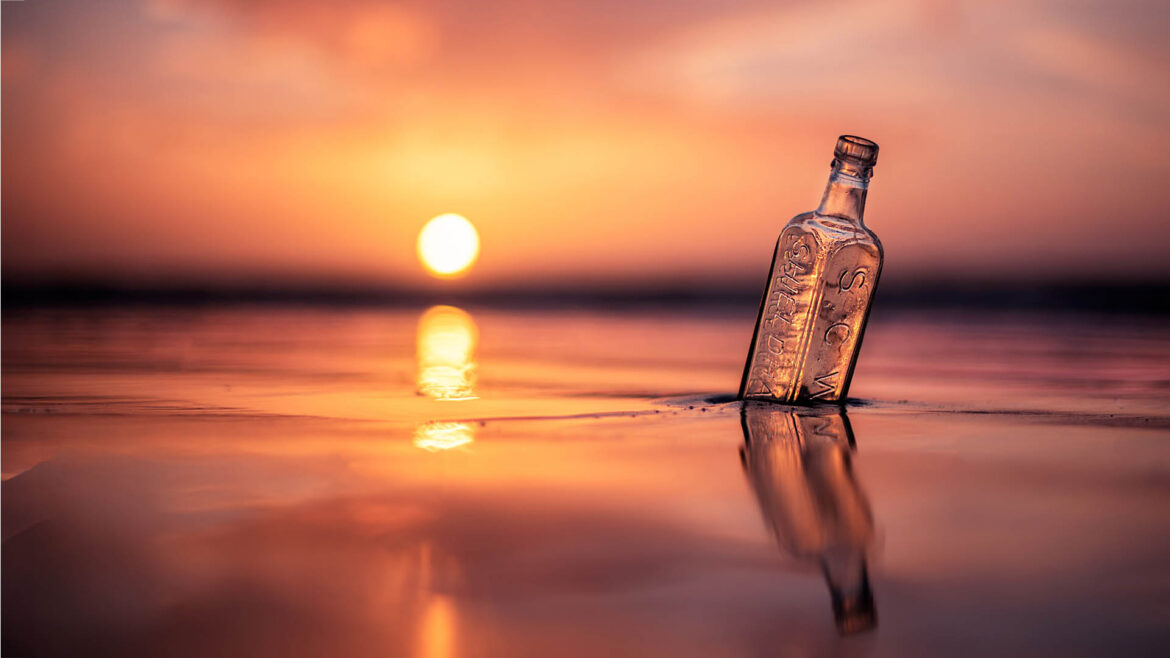 Antique bottle on the beach partly sunken into the sand with the setting sun in the background