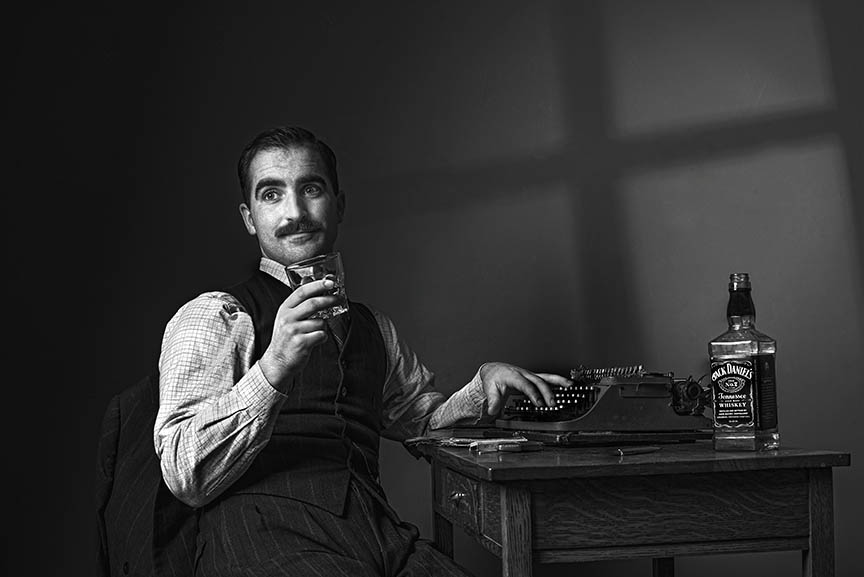 Vintage-inspired scene with a man in 1920s attire typing on an old typewriter, a glass of whiskey by his side, capturing the essence of film noir.