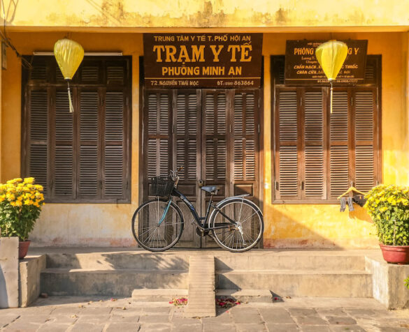 A bicycle parked in front of a yellow building with brown shutters in Hoi An, Vietnam