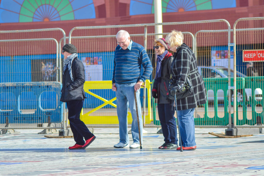 Clear, focused photograph of three people walking and engaging in conversation on a sunny street with vibrant colors and distinct shadows.