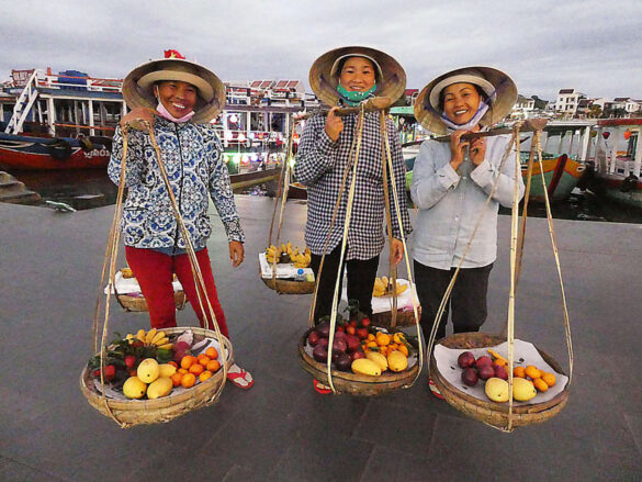 Cheerful fruit sellers in Hanoi, Vietnam with traditional carrying poles