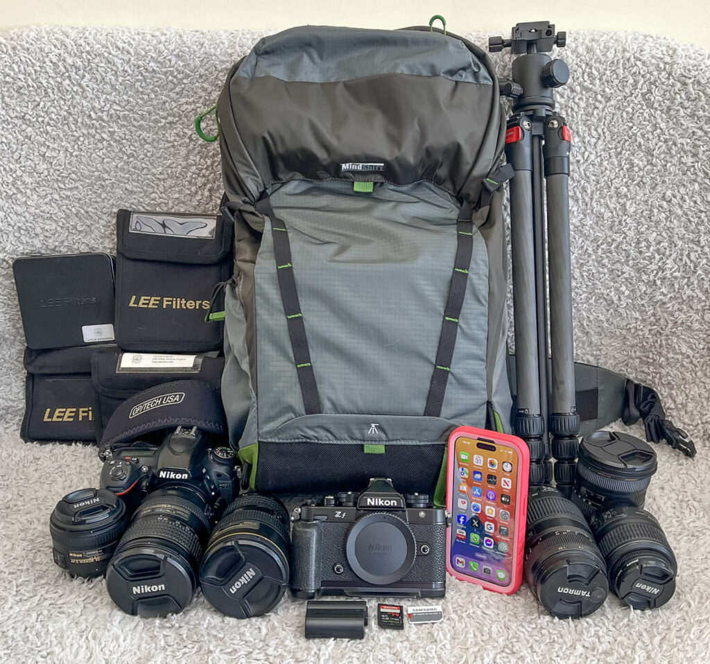 An assortment of photography equipment neatly arranged, including a Nikon camera body, several lenses, a tripod, filters, and a smartphone, all ready for a photography adventure