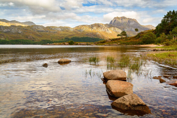 Stunning view of Beinn Eighe mountain and peaceful loch with rocks in the foreground