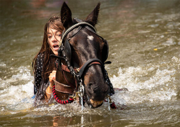 Dark-haired girl riding a horse through water at Appleby Horse Fair.