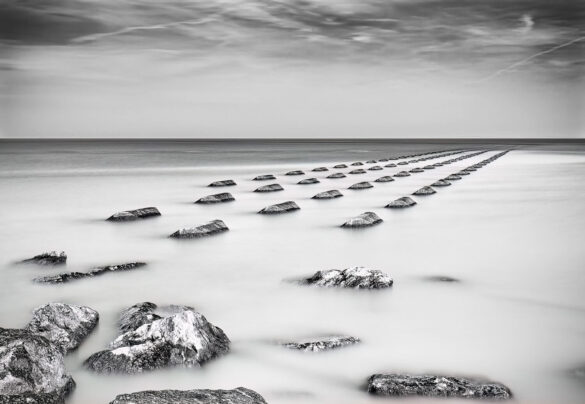 Monochrome image of stones in the ocean creating ethereal lines.