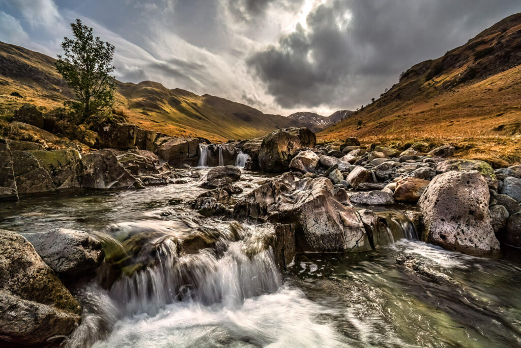 Rocky stream with flowing water and mountains in the background.