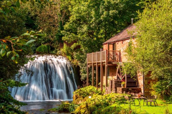 Picturesque waterfall with a stone house beside it, surrounded by lush greenery