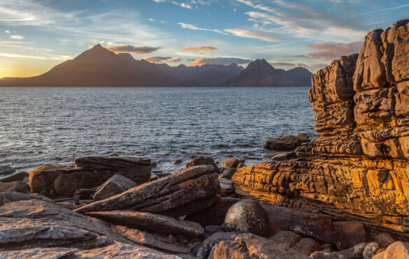 Rocky shoreline with a view of The Black Cuillins at sunset.